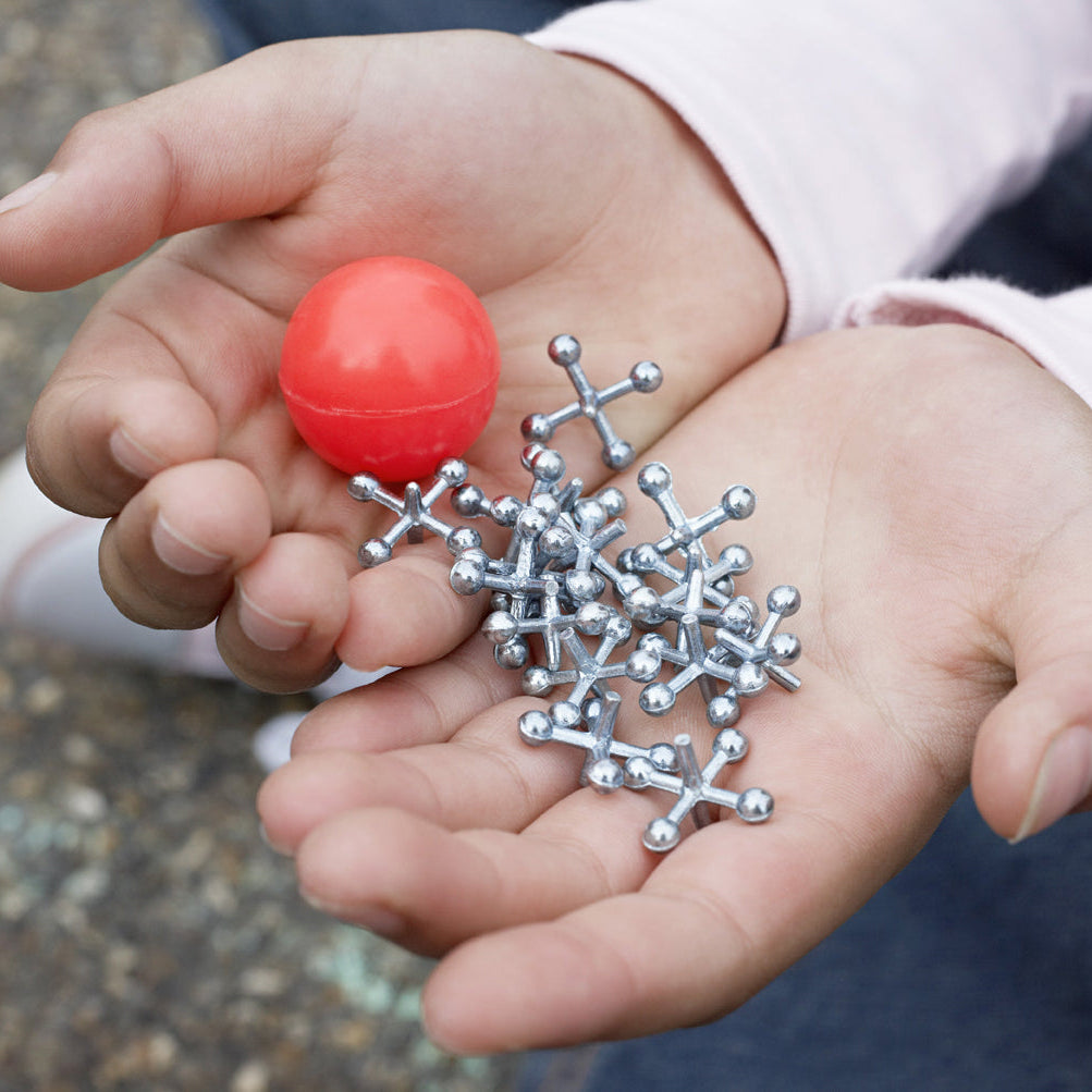 A close-up of two hands holding a small red spherical toy and several metallic silver molecular model balls, with a child's light pink sleeve visible in the background.